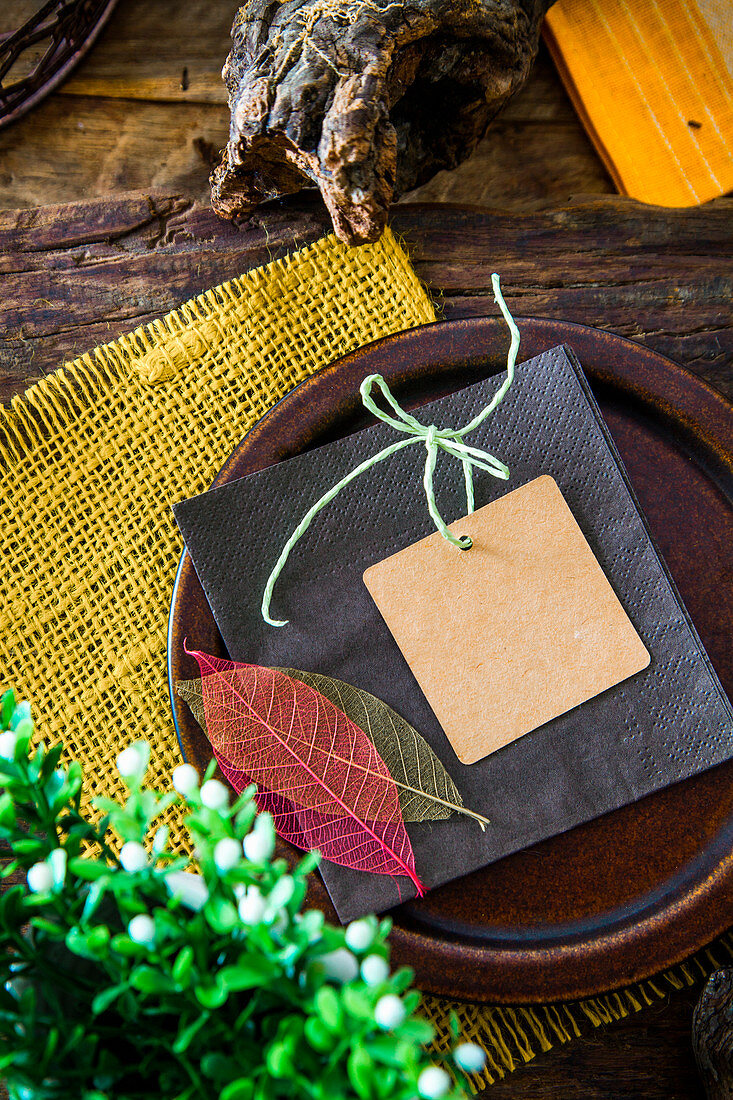 Place setting with a card and leaf decorations on a rustic wooden table