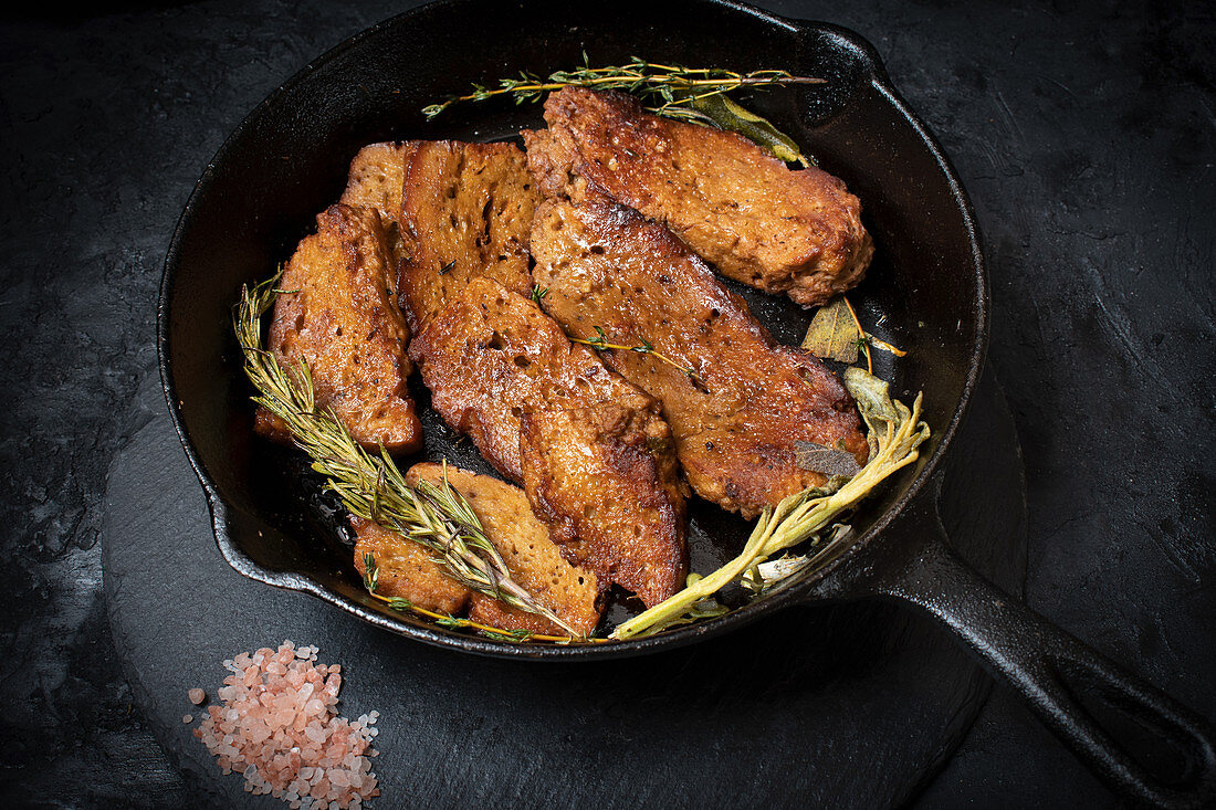 Roasted seitan in cast iron pan with various herbs and spices