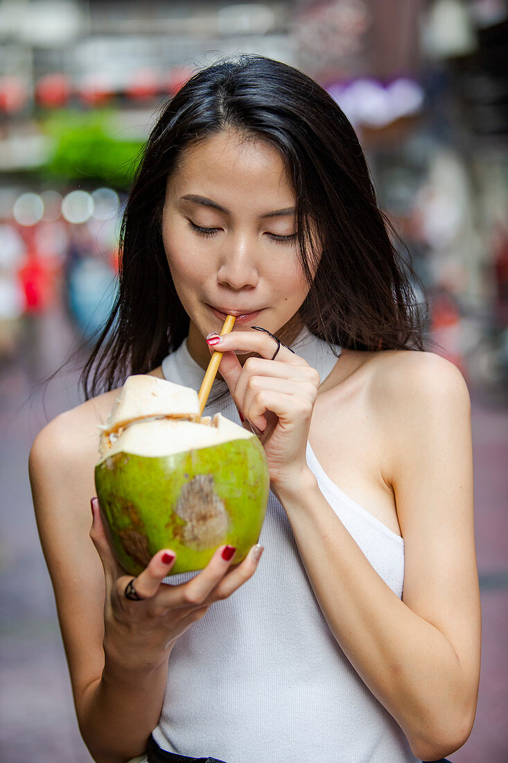 Junge Asiatin trinkt frisches Kokoswasser aus einer Kokosnuss