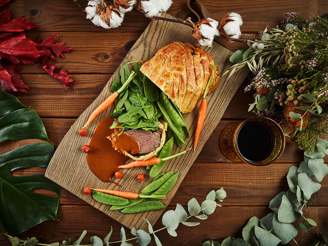 Wellington sirloin served with fresh vegetables and red wine on lumber tabletop