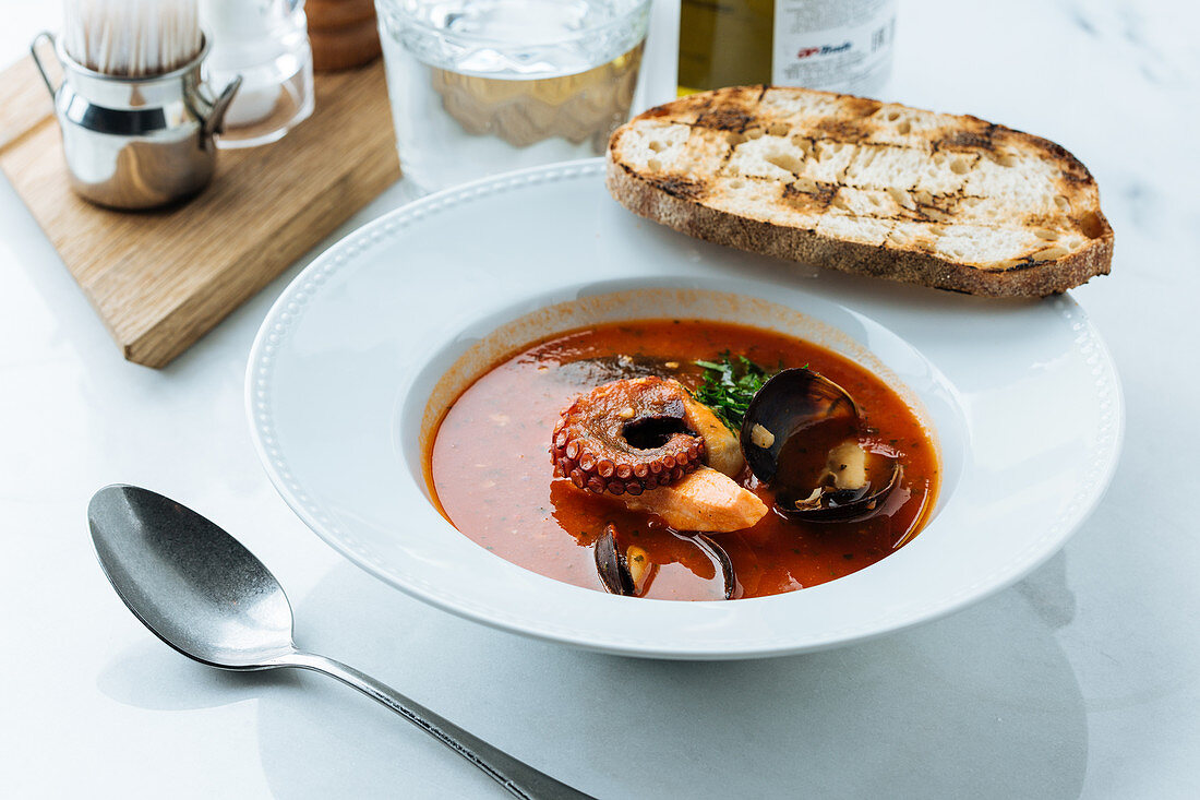 Red soup of octopus and mussels served with greenery and roasted bread