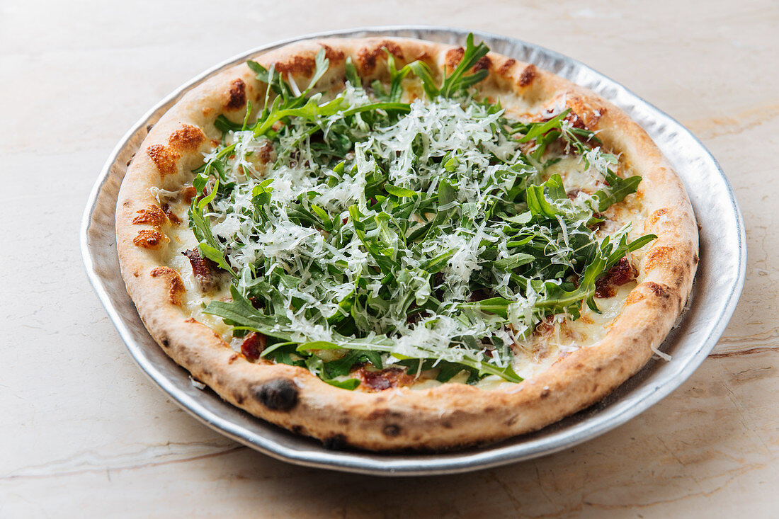 Baked pizza decorated with green arugula and grated cheese