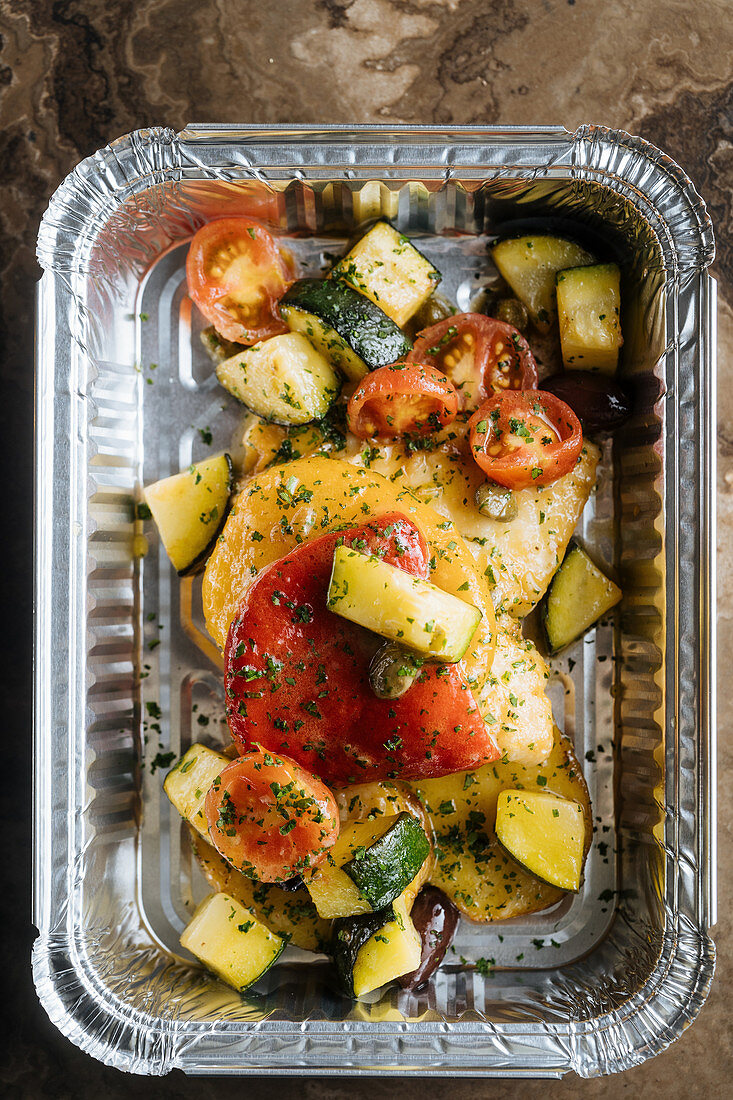 Slice red tomatoes, zucchini sprinkled with herbs and sauces in shiny baking form