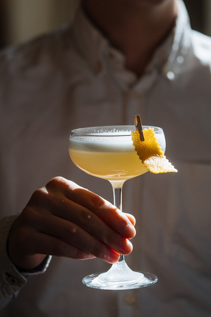 Cropped person holding fresh appetizing cocktail in glass festively decorated with clothespin