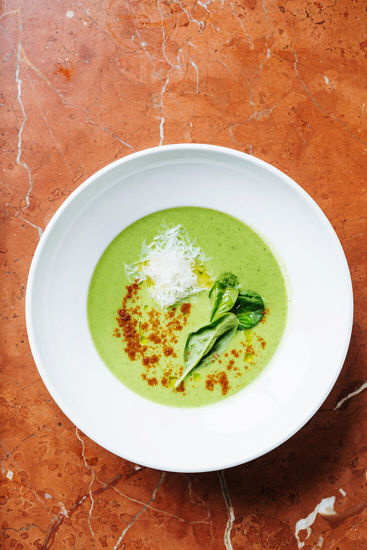 Cream soup of broccoli in white bowl with leaves of fresh basil and spices
