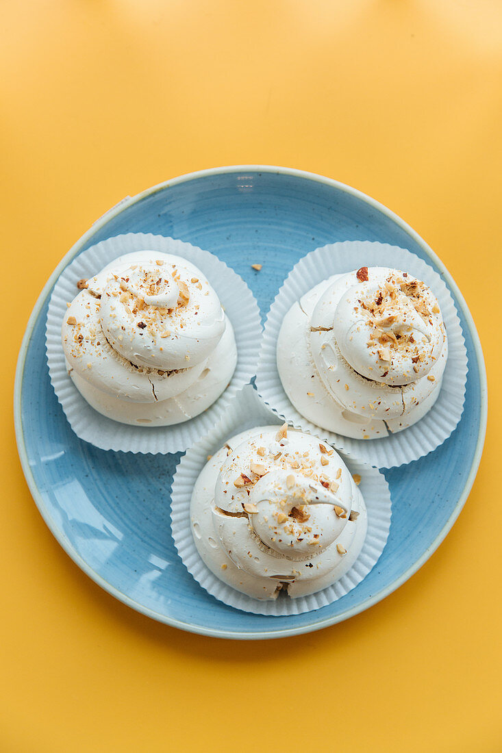 Creamy meringue with pieces of nuts in blue ceramic plate on yellow table