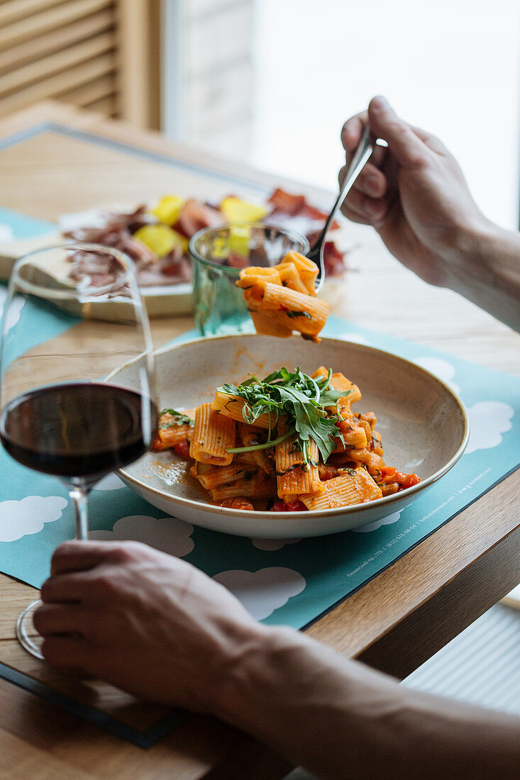 Mann isst vegane Nudeln mit Sauce und Rucola im Restaurant