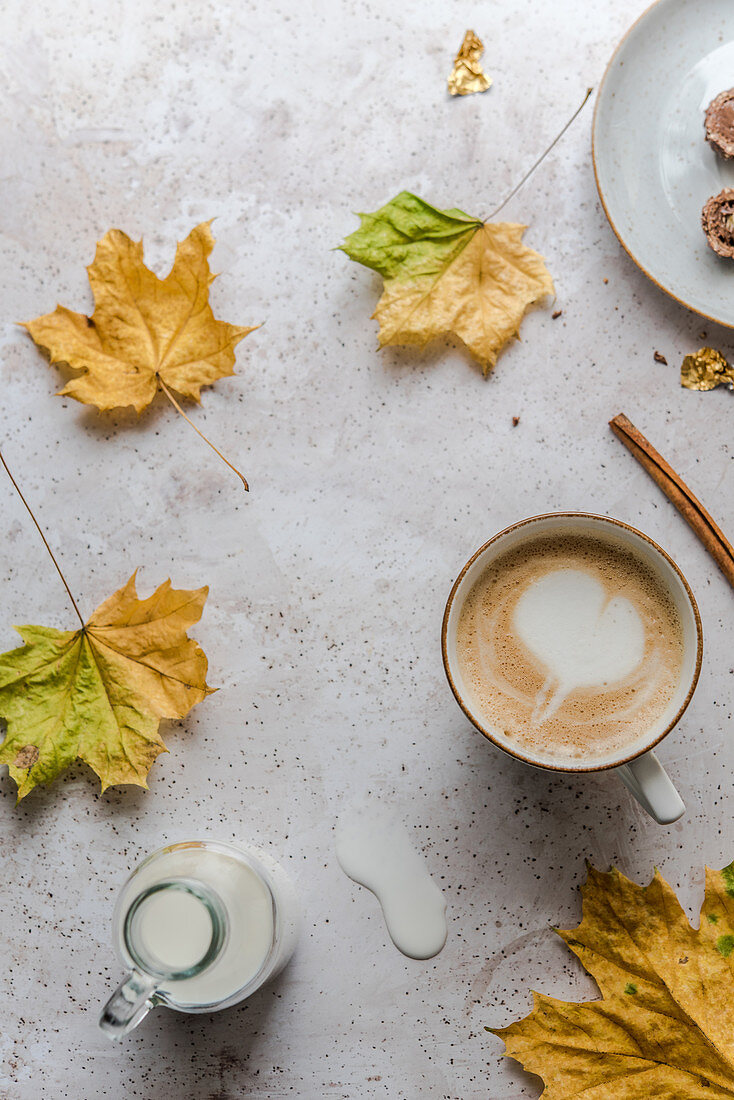 Cappuccino with a milk foam heart surrounded by autumn leaves