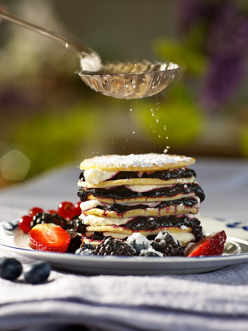 Powdered sugar dusted on a pancake stack with berries and cream