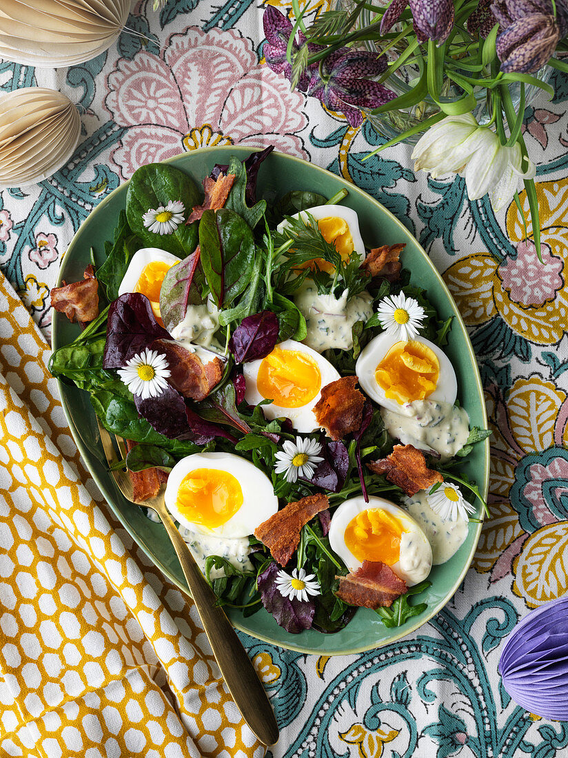 Blattsalat mit gekochten Eiern, Speck und Gänseblümchen