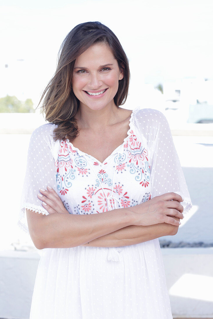 A long-haired woman wearing a white summer dress with colourful embroidery detail