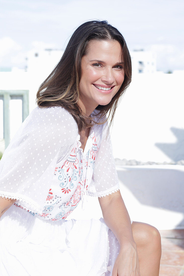 A long-haired woman wearing a white summer dress with colourful embroidery detail