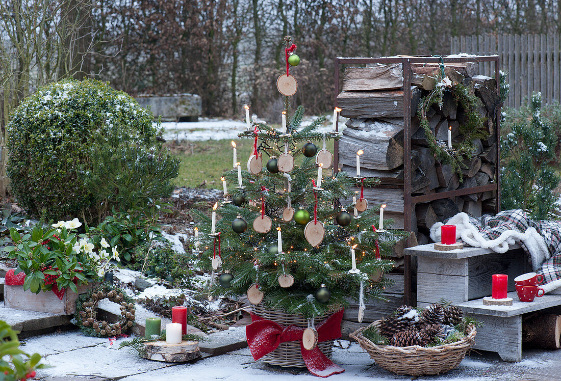 Nordmanntanne geschmückt mit Holzscheiben, Christbaumkugeln, Lichterkette und Kerzen, Korb mit Zapfen