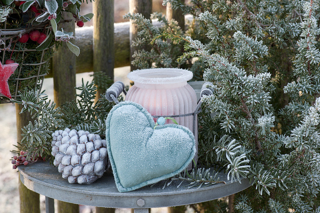 Side table with lantern, heart and cones as a welcome to the garden fence, frozen over with hoarfrost