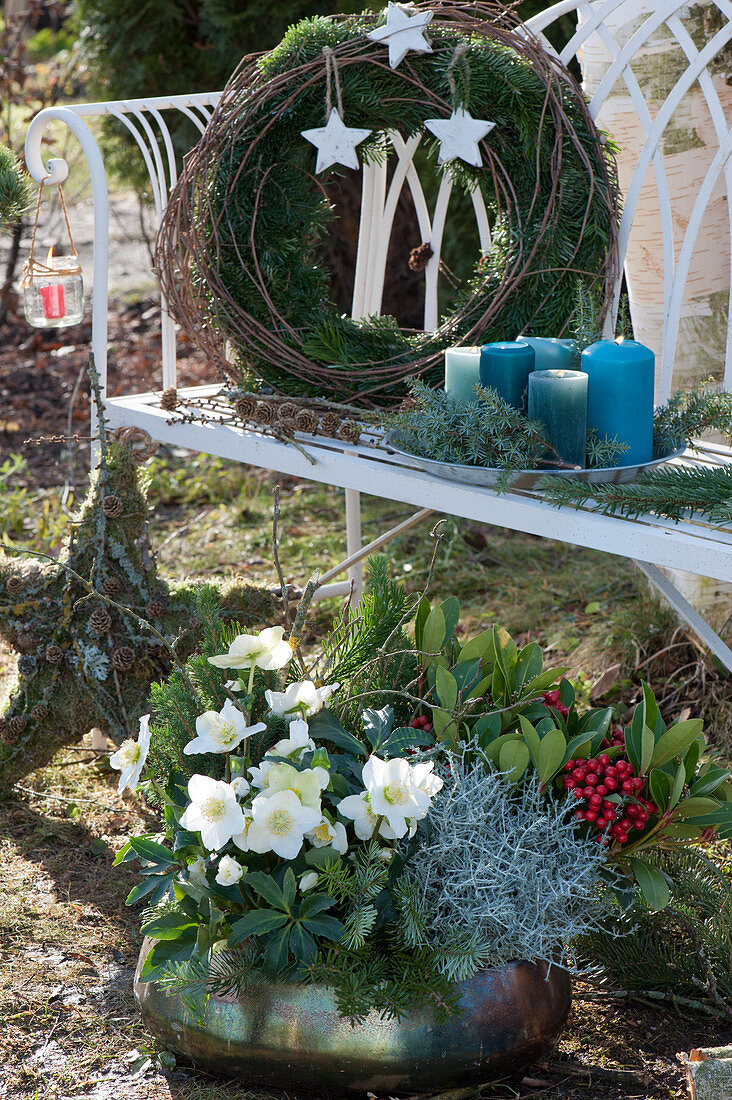 Weihnachtliches Arrangement mit bepflanzter Kupferschale, Kranz, Kerzen und Stern an Gartenbank