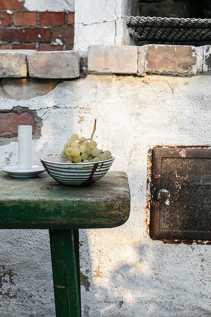 Schale mit Trauben auf abgenutztem grünen Hocker vor alter Mauer