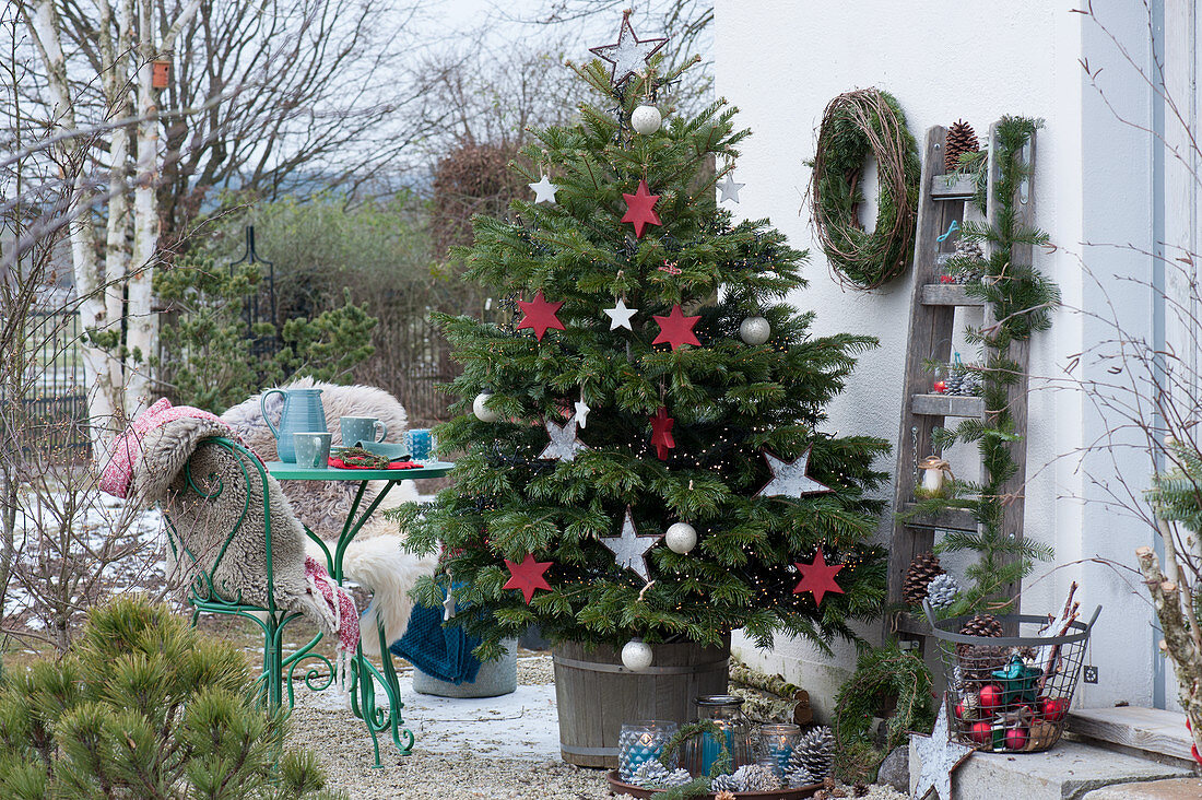 Nordmann fir decorated with stars and balls as a Christmas tree on the terrace, small seating area, chairs with fur