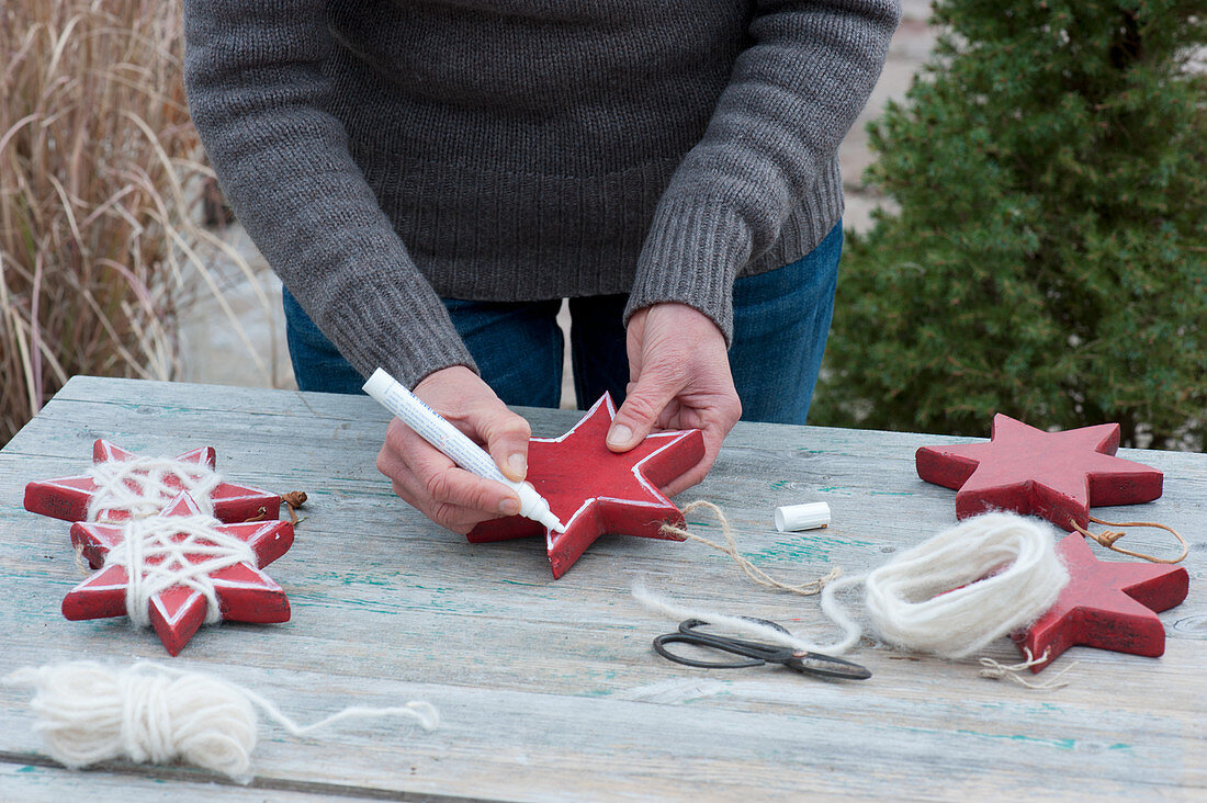 Woman paints red wooden stars with white paint pen
