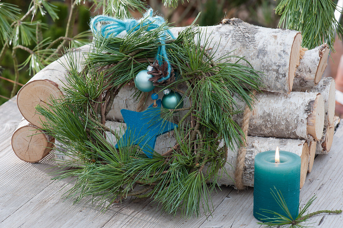 Wreath of pine branches with a star, balls and ribbon leaning against birch trunks
