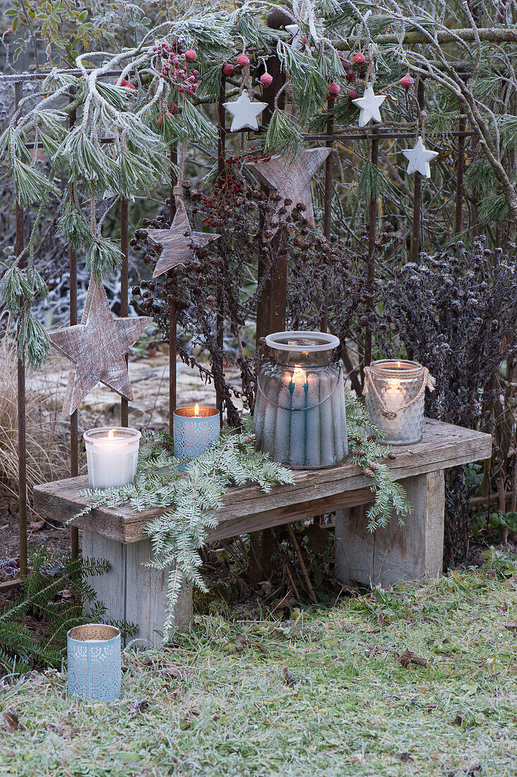 Christmas arrangement with lights and hoarfrost on the garden fence, wooden stars on a pine branch