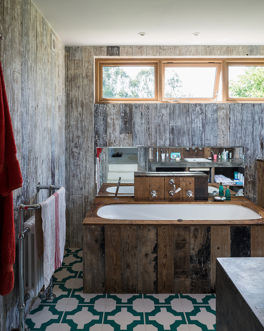 Bathtub with reclaimed-wood surround in rustic bathroom with board wall