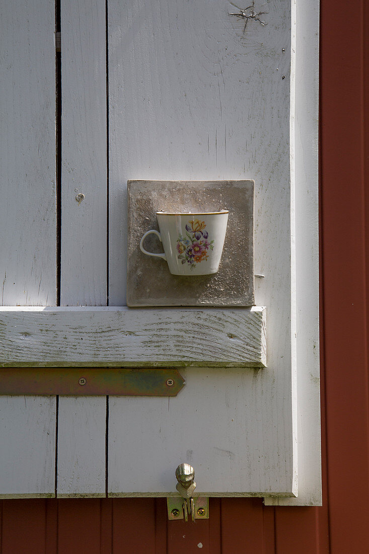 In Beton eingelassene Tasse als Windlicht auf einem Fensterladen