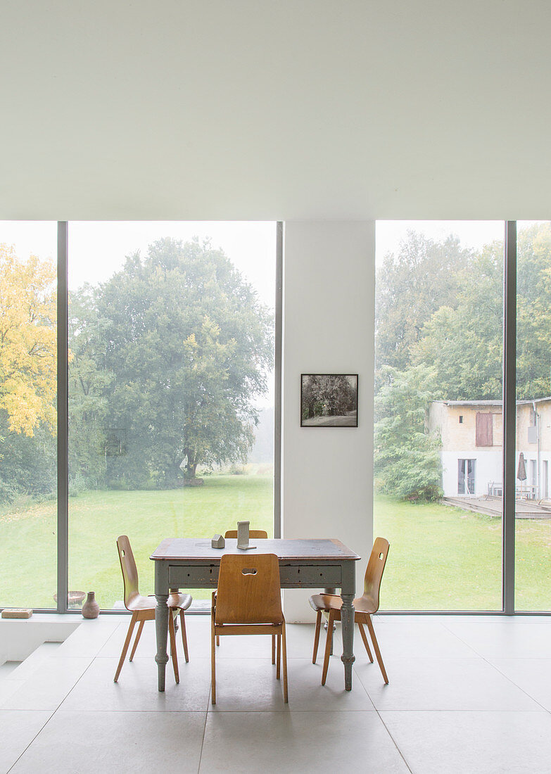 Stühle am alten Holztisch vor der Fensterfront mit Blick in den Garten