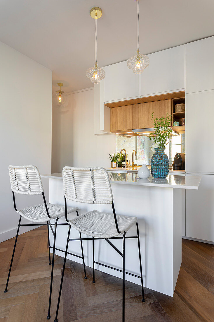 Barstools at island counter in small, white, open-plan kitchen