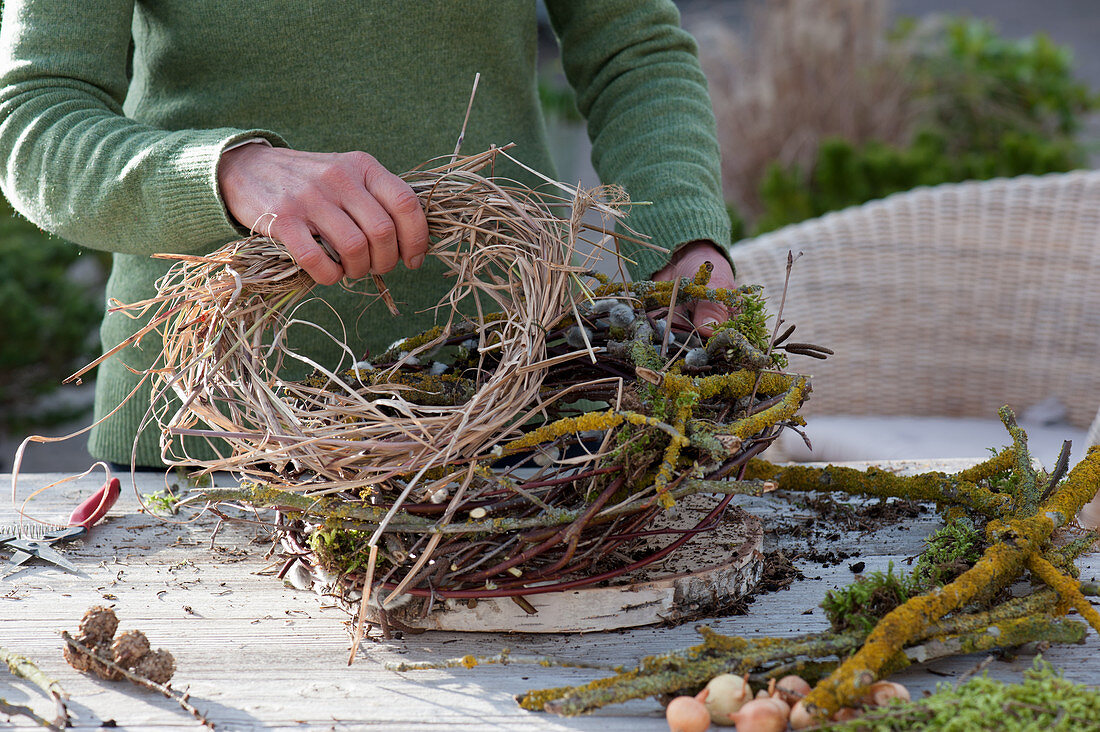 Snowdrops in a wreath of twigs: Woman puts snowdrops in moss in a lichen-covered twigs wreath, birch, willow and grass