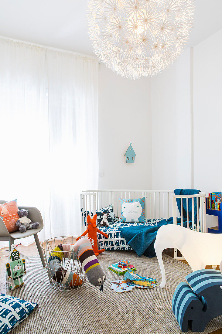 Cot and colourful toys in light-flooded child's bedroom