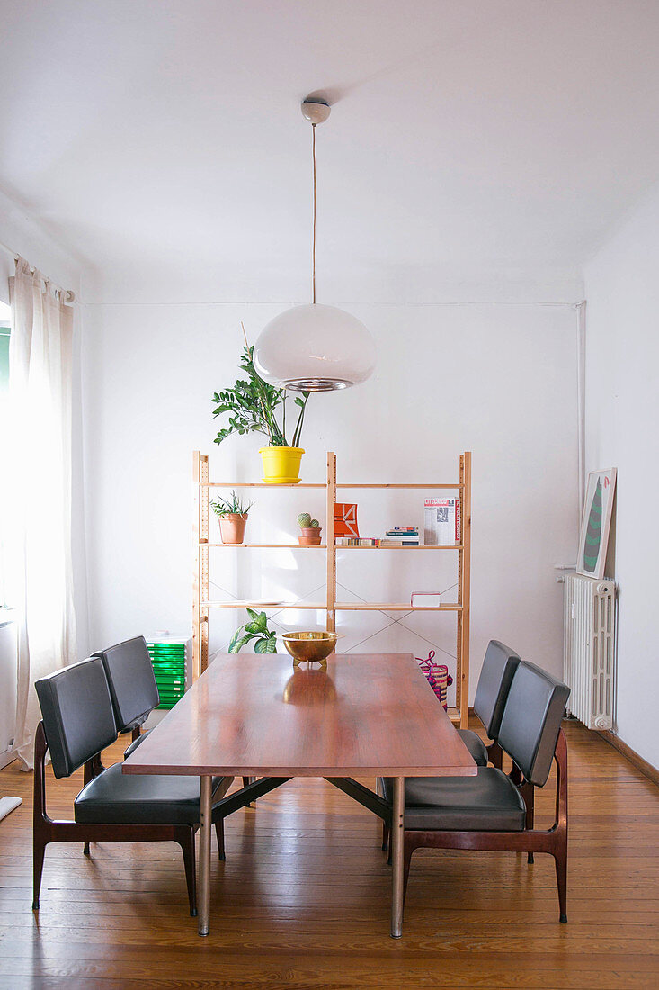 Dining table and black leather chairs in front of shelves