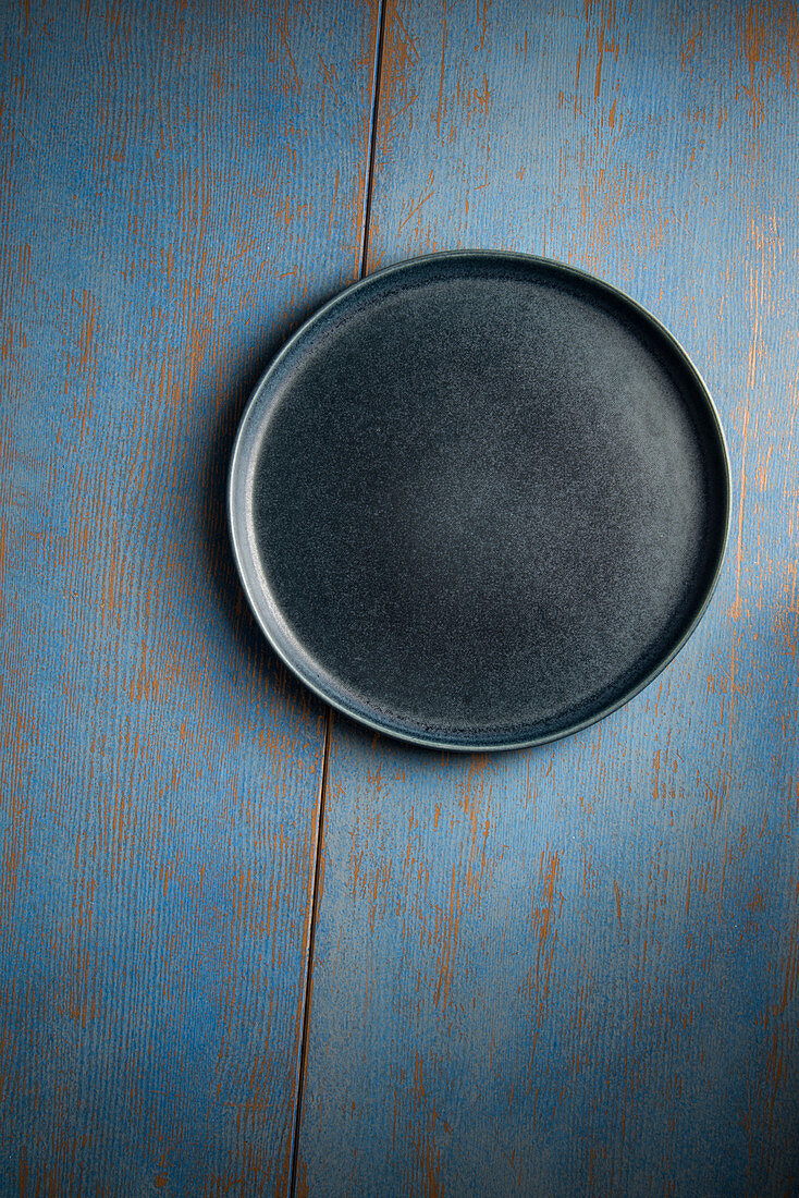 An empty blue plate on a blue wooden surface