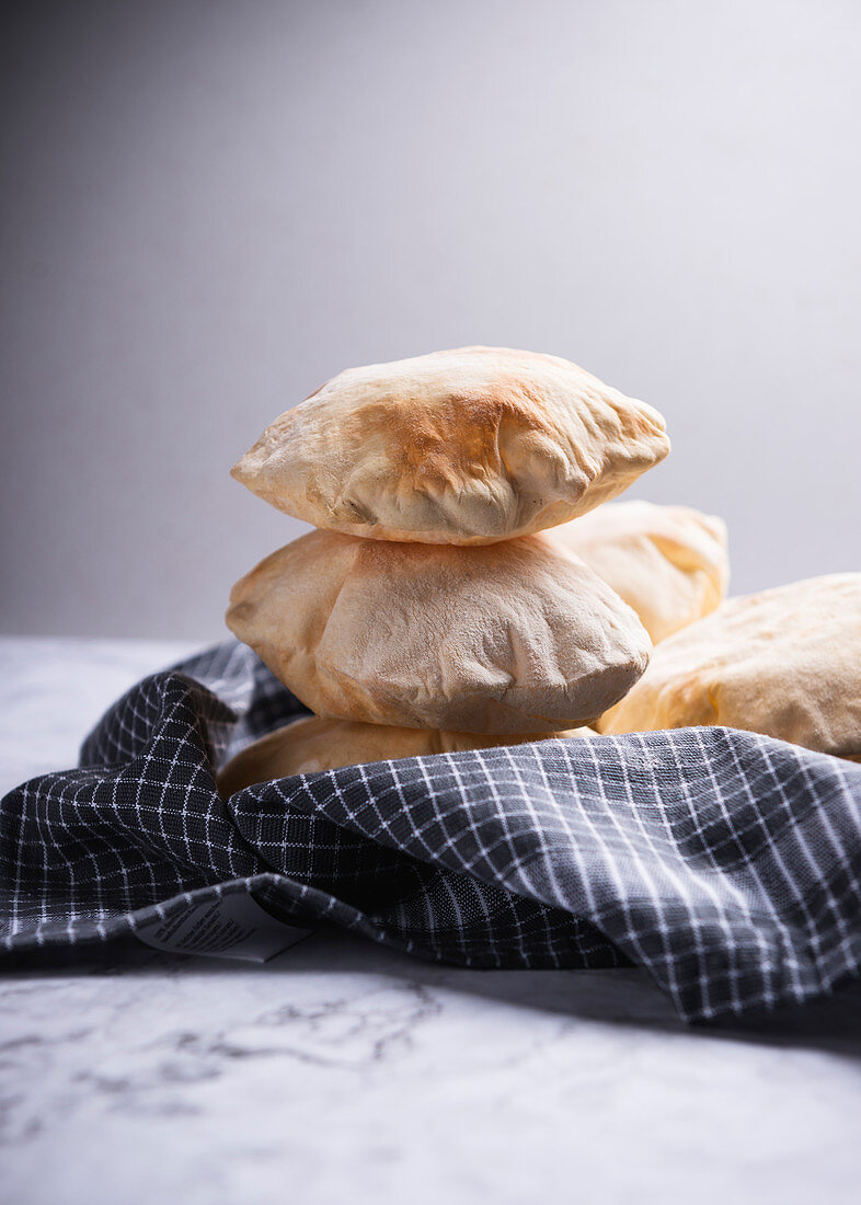 Pita bread stacked on a tea towel against a grey background