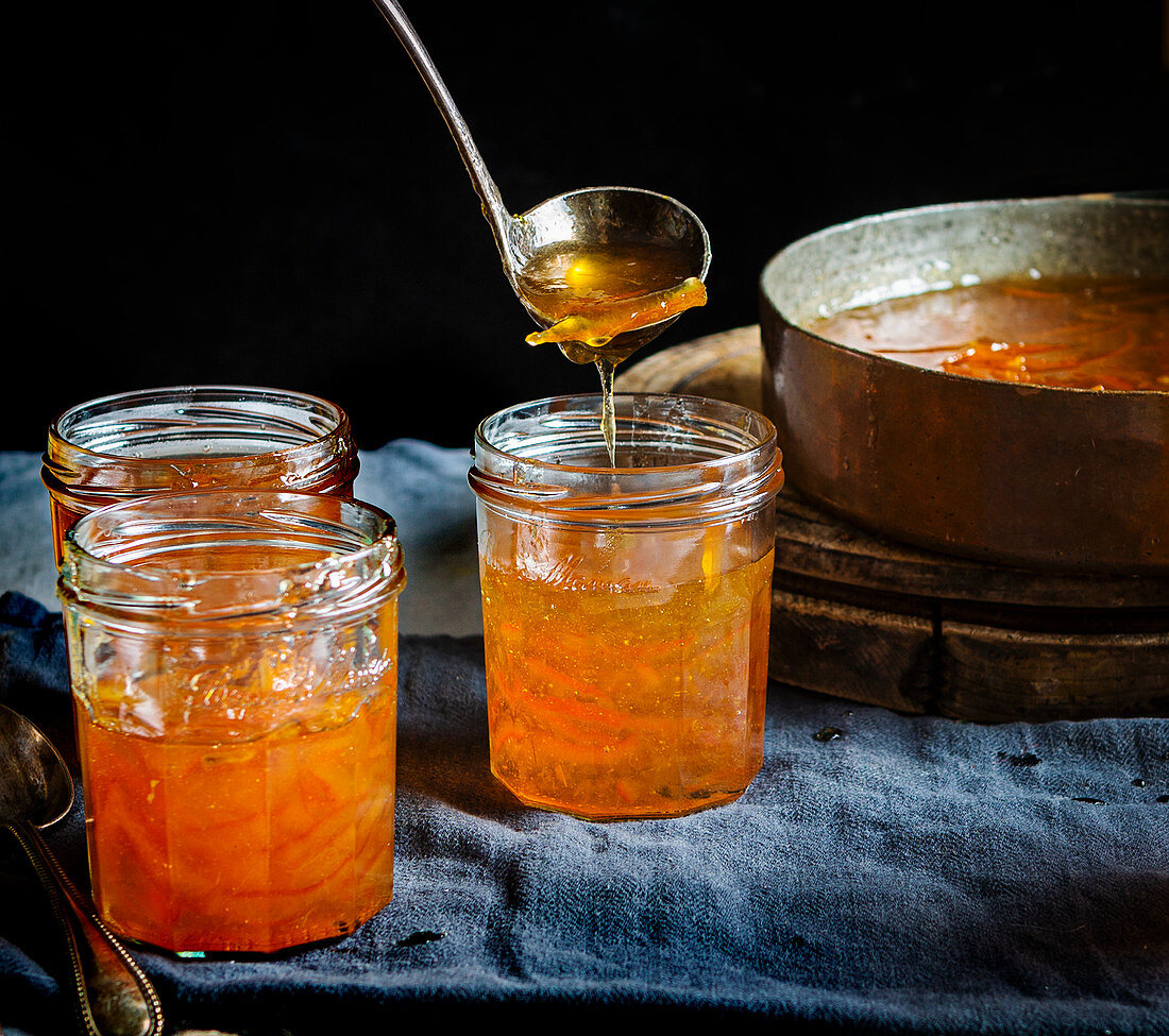 Pouring orange jam from Seville oranges into glasses