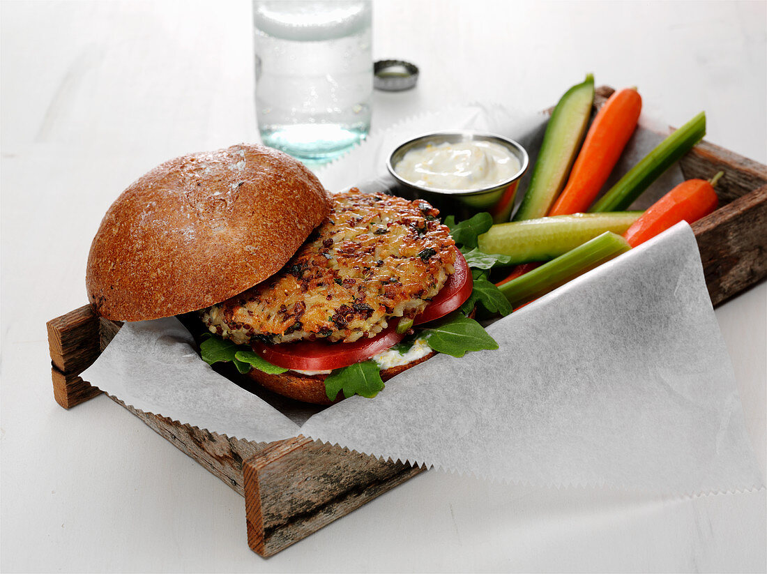 Quinoa and brown rice burger with tomato and baby spinach on a bun with vegetable spears
