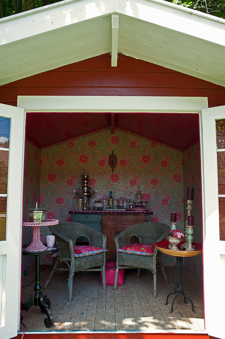 Floral wallpaper, side tables and wicker chairs in summerhouse