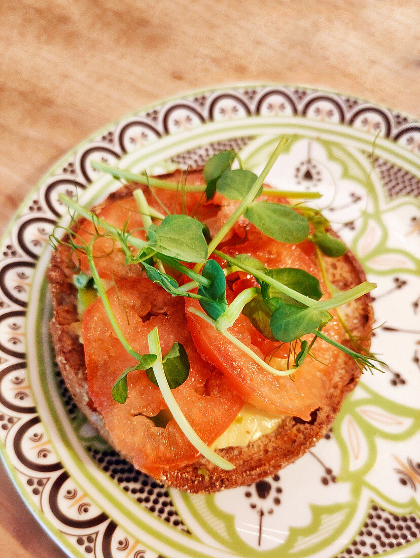 A bread roll topped with tomatoes and pea sprouts