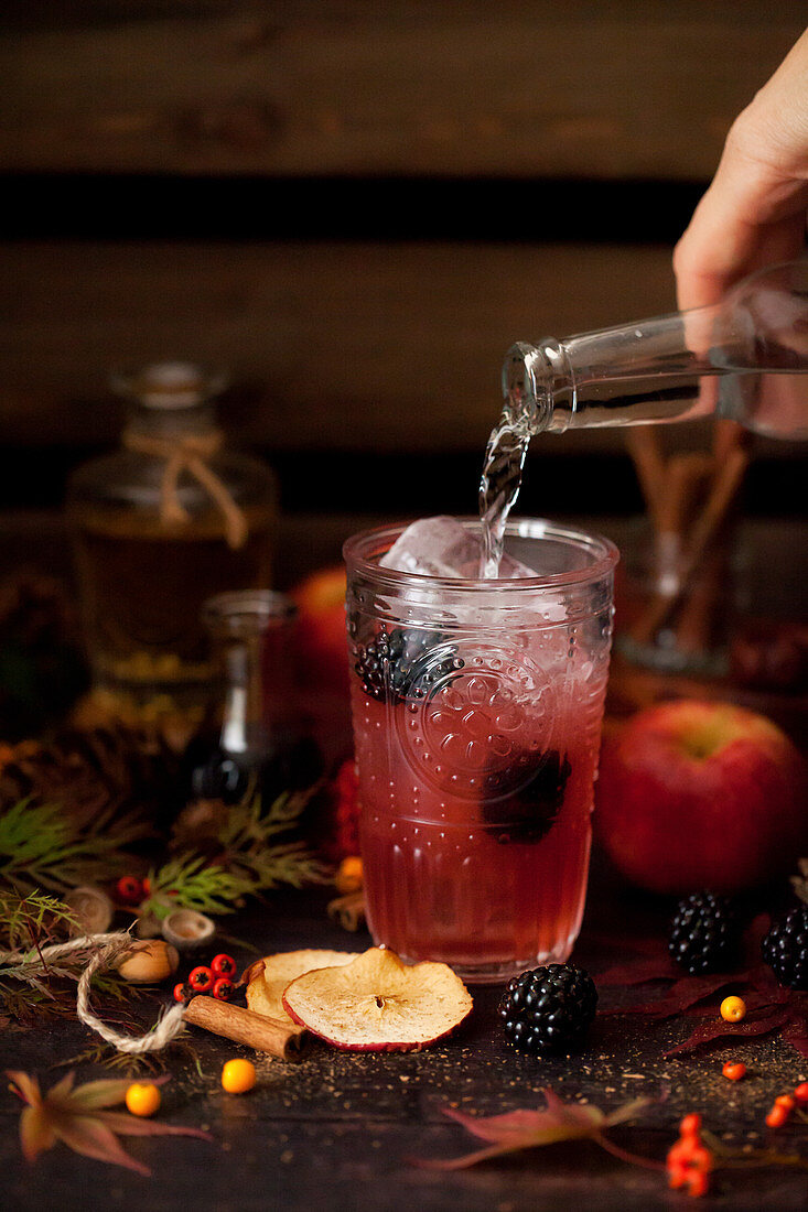 Pouring tonic water into an apple and blackberry gin and tonic