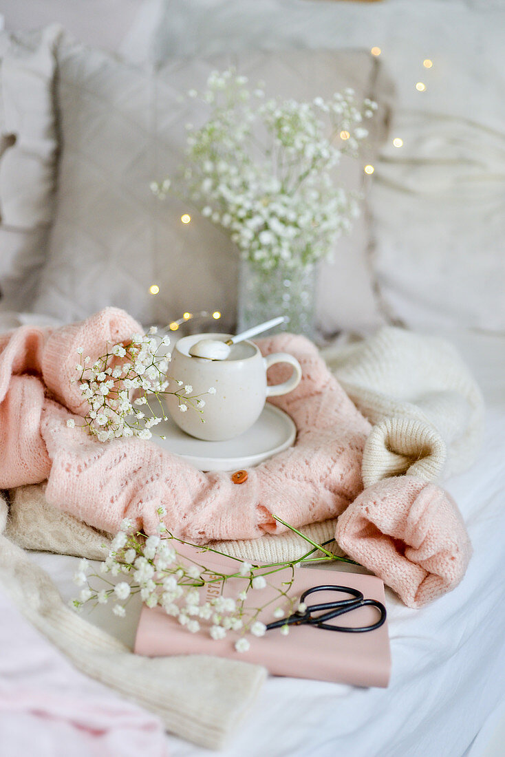 Kaffeetasse mit Zuckerlöffel auf Strickweste im Bett