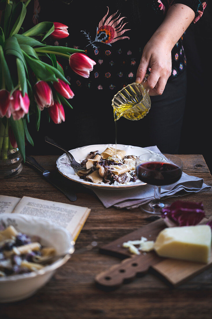 Woman drizzling olive oil over pasta with radicchio, panceta and Parmesan