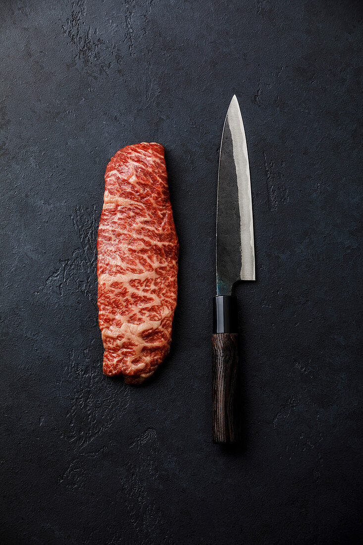 Marmoriertes rohes Steak vom Wagyu-Rind mit Messer auf dunklem Untergrund
