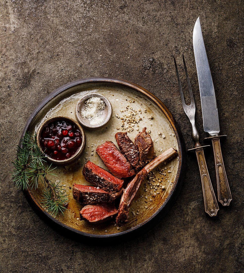 Grilled sliced Venison Ribs and berry sauce on dark background