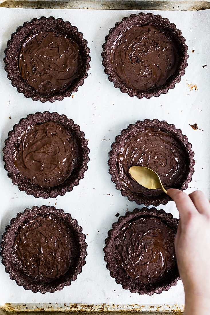 Chocolate tartlets being made: tart bases being spread with chocolate
