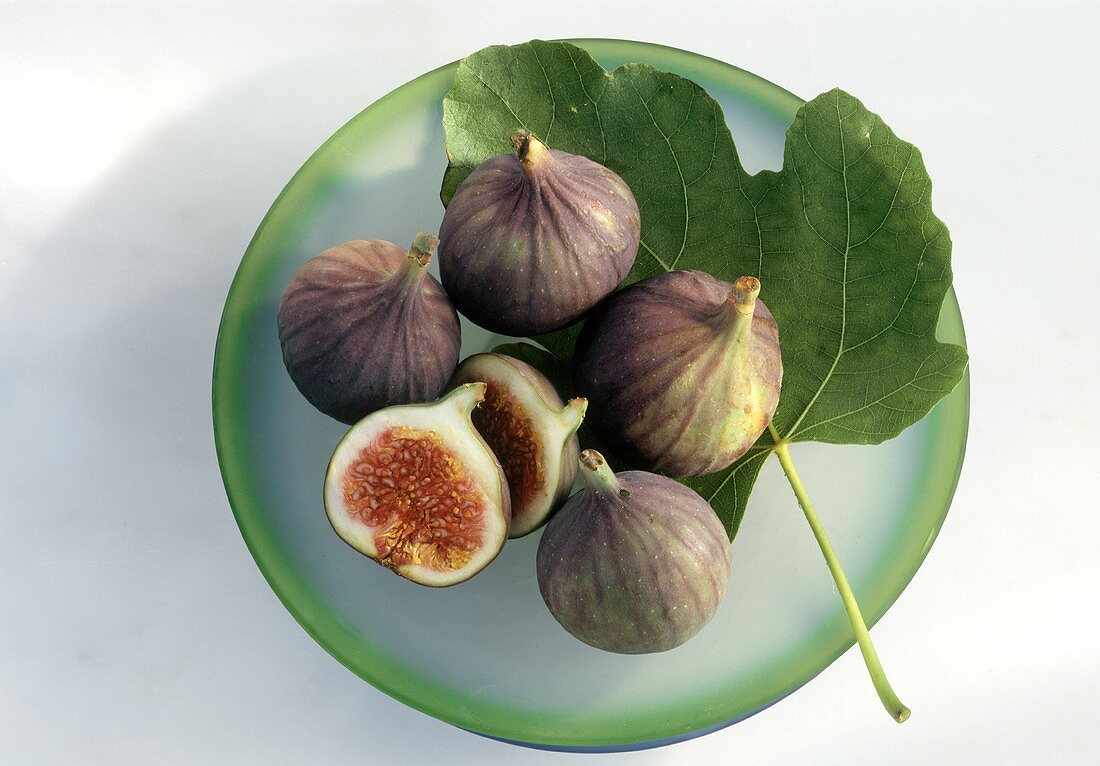 Five figs, one halved, on plate with fig leaf
