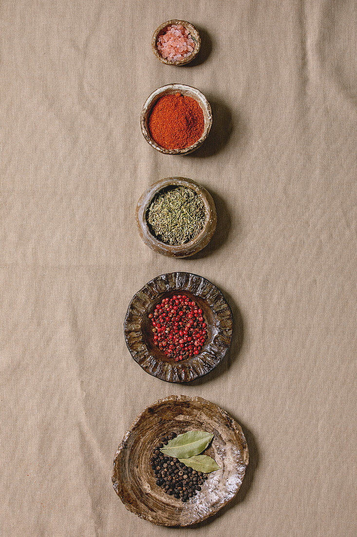Variety of different handmade ceramic plates and bowls in row with seasonings and spices