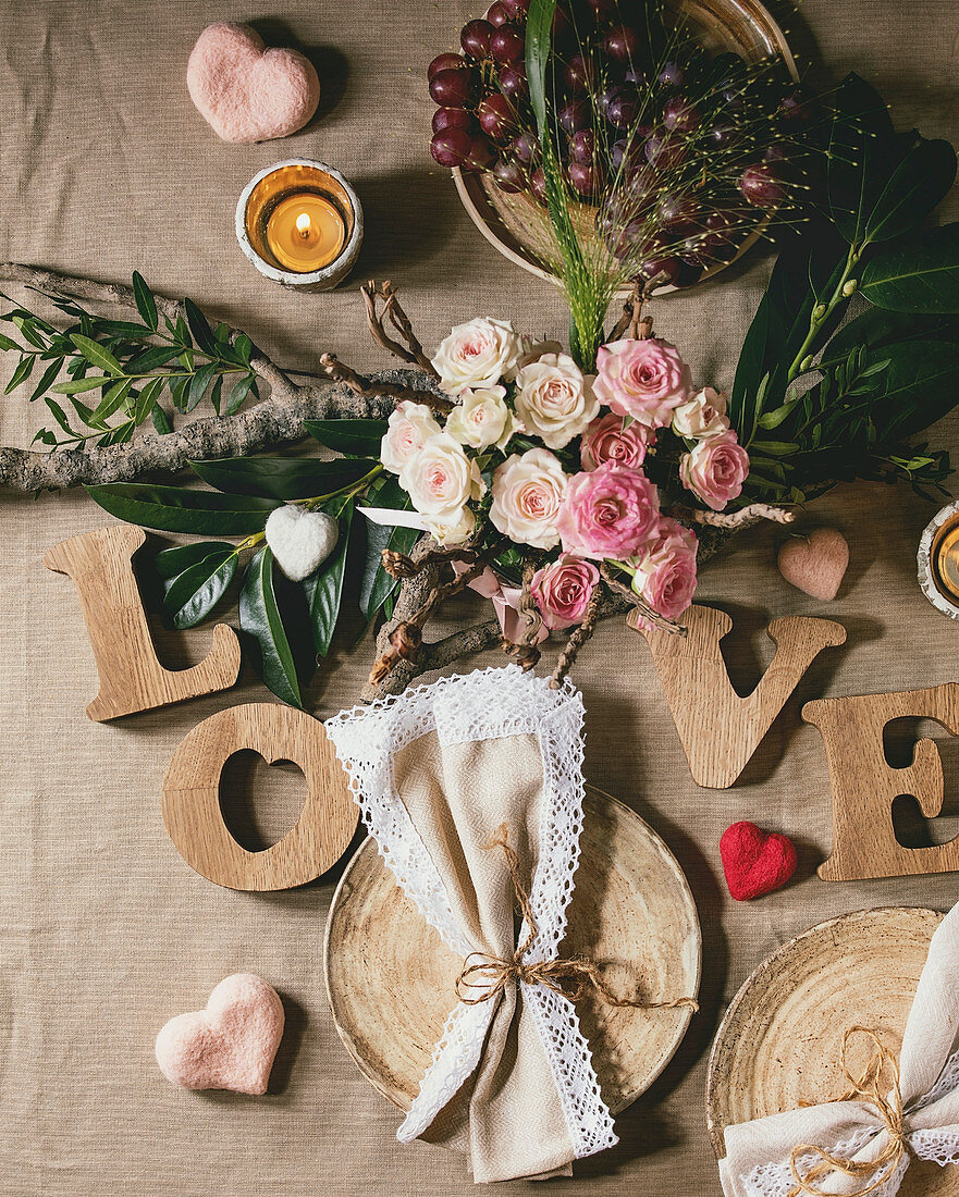 Romantische Tischdeko zum Valentinstag mit Rosenstrauß und dem Wort 'love' aus Holzbuchstaben