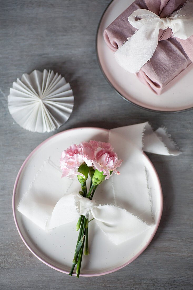 Deko in Pastell: Nelken in Rosa mit Stoffband auf einem Teller