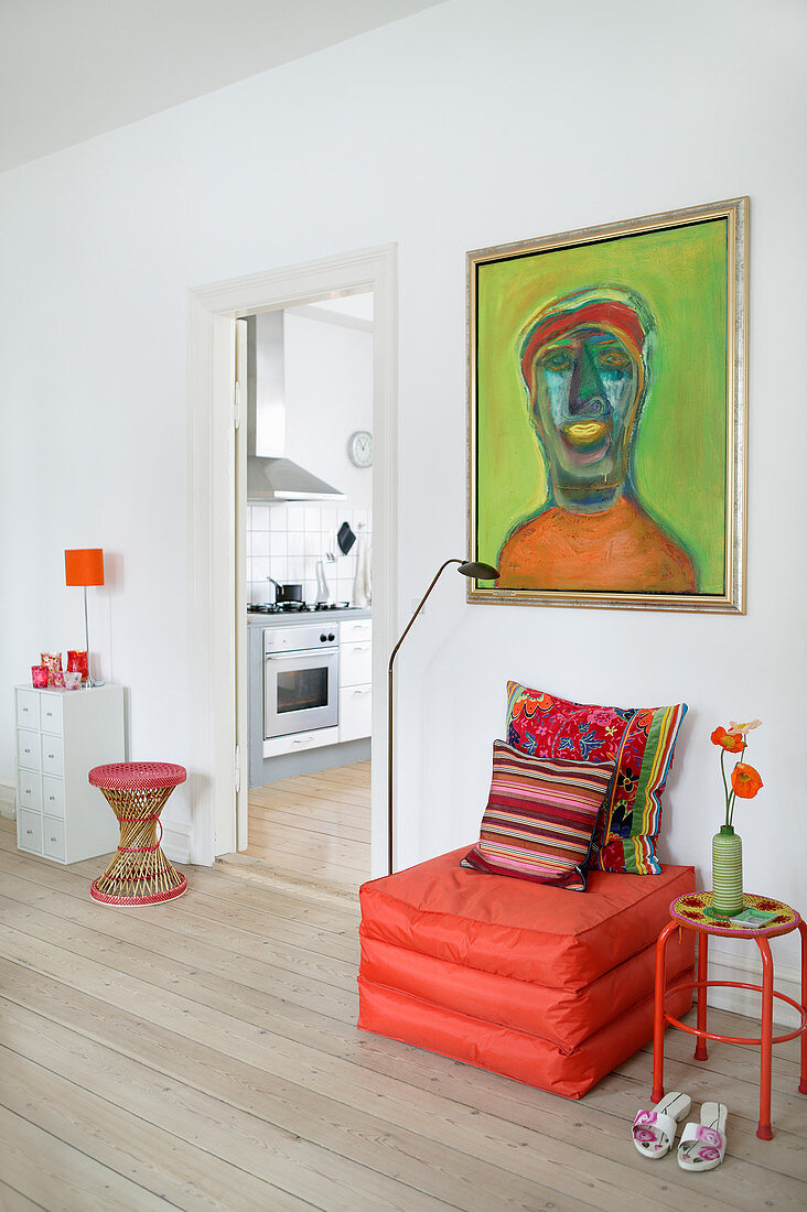 Orange pouffe below green painting in living room