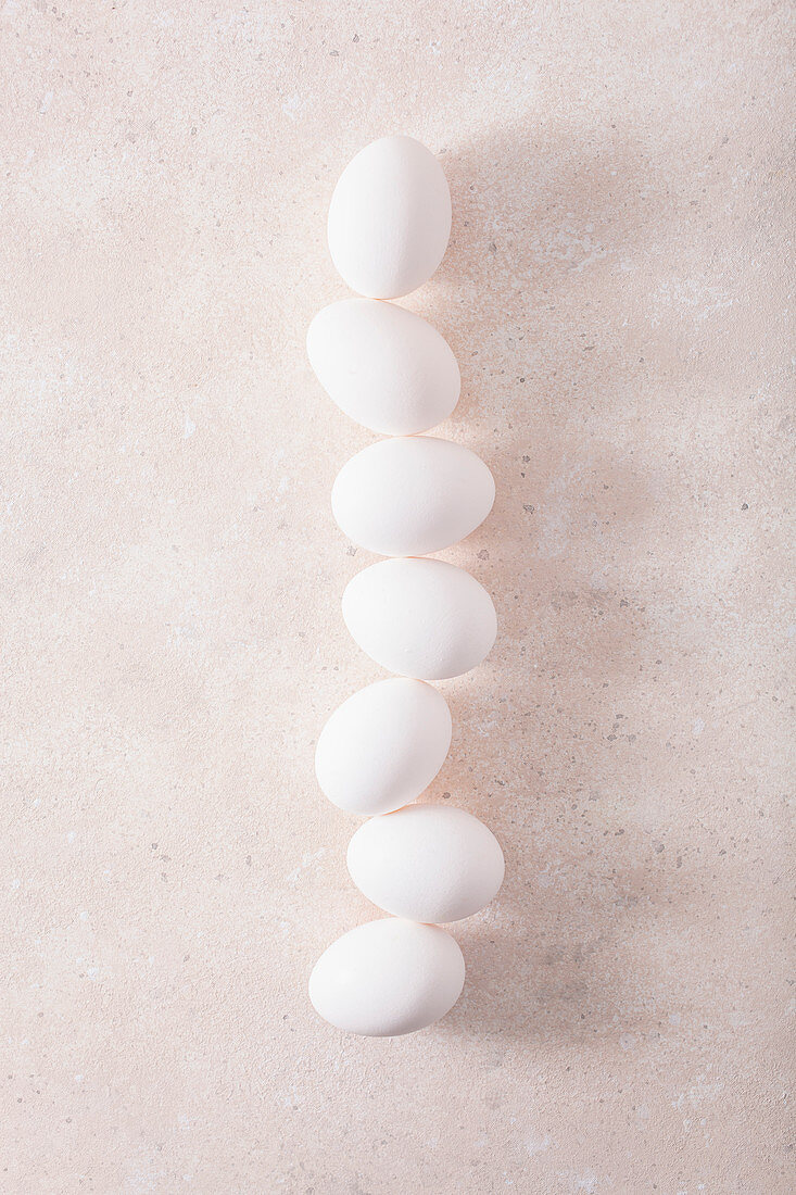 Seven white hen's eggs in a row on a light surface