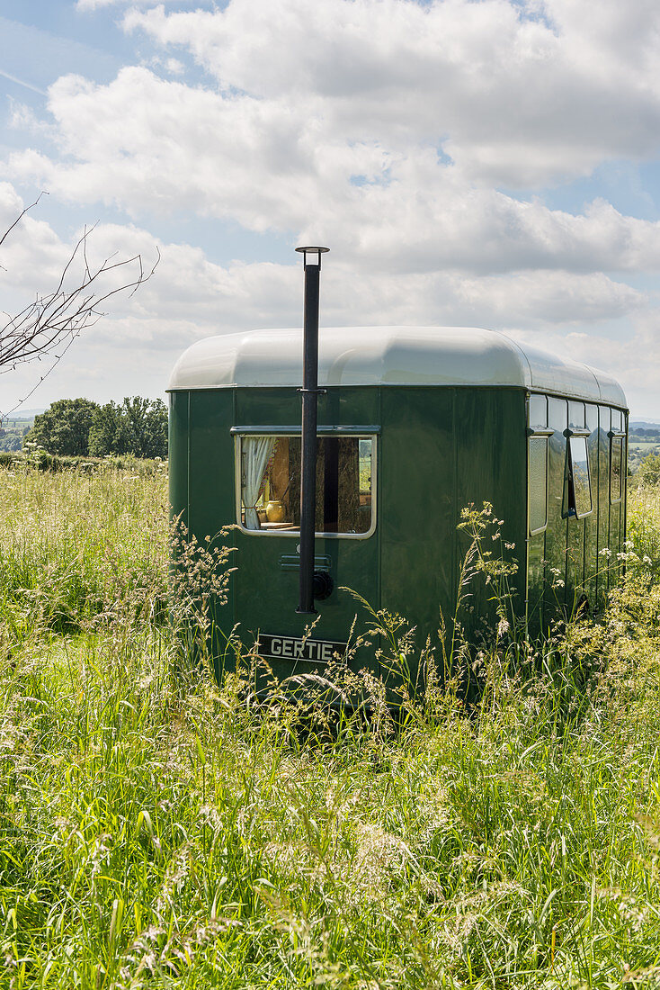 Vintage-style green caravan with chimney in summery meadow